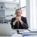 Smiling businessman in a suit with laptop and documents, exuding confidence.